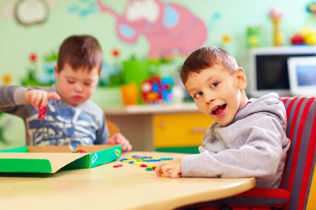 cute kids with special needs playing with developing toys while sitting at the desk in daycare center cute kids with special needs playing with developing toys while sitting at the desk in daycare center